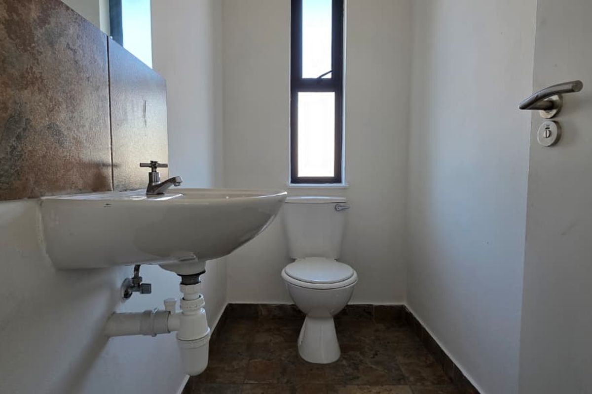 A compact bathroom featuring a wall-mounted basin with tiled splashback, a standard toilet, and tiled flooring with a vertical window for natural light.