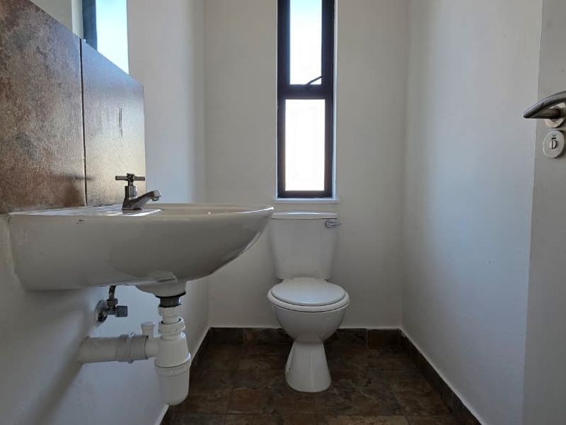 A compact bathroom featuring a wall-mounted basin with tiled splashback, a standard toilet, and tiled flooring with a vertical window for natural light.