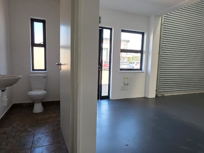 Industrial unit featuring a spacious warehouse area with a roller shutter door, adjacent to a private restroom facility with a basin and toilet.