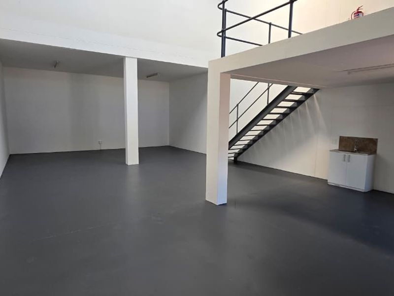Spacious industrial open-plan unit featuring a mezzanine level, metal staircase, and a compact kitchenette, offering versatile workspace potential.