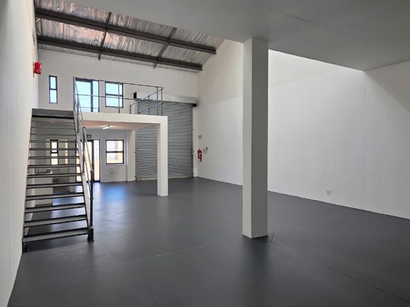 Spacious industrial open-plan unit featuring a mezzanine level, metal staircase, roller shutter door, and durable epoxy flooring, suitable for various commercial or storage uses.