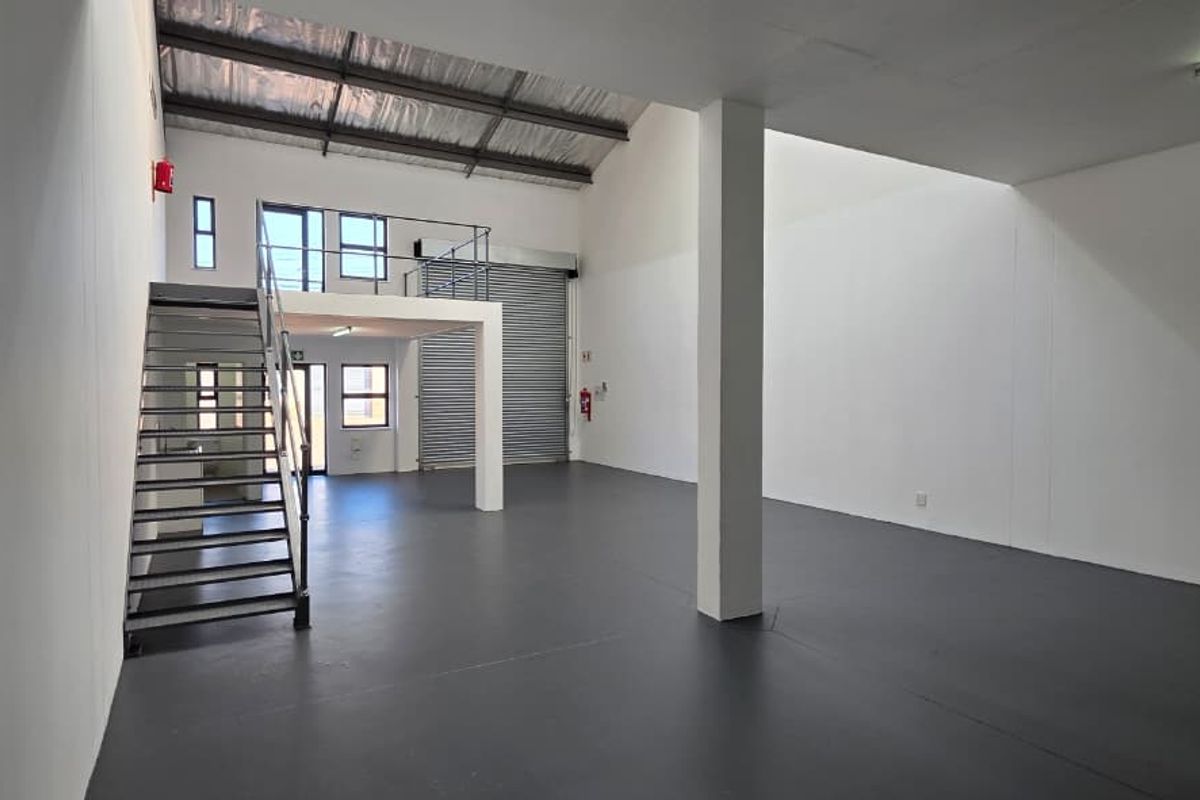 Spacious industrial open-plan unit featuring a mezzanine level, metal staircase, roller shutter door, and durable epoxy flooring, suitable for various commercial or storage uses.