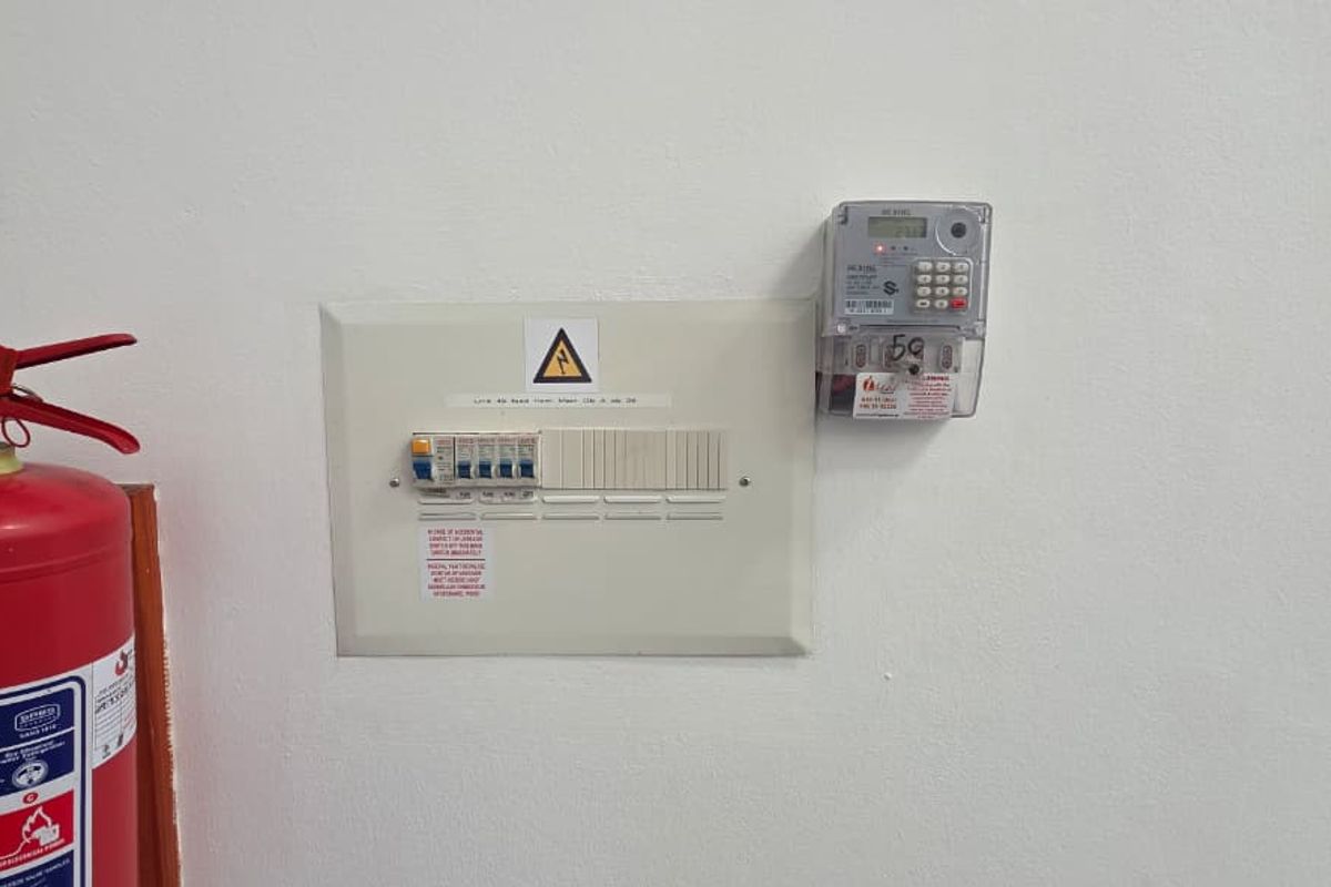 Wall-mounted electrical distribution board and prepaid electricity meter, accompanied by a fire safety extinguisher in a clean utility area.