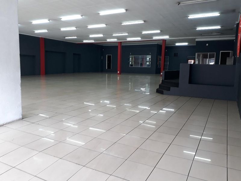 A spacious, open-plan commercial interior featuring tiled flooring, recessed fluorescent lighting, and a raised platform area, suitable for retail or office use.