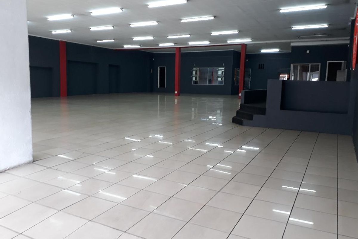 A spacious, open-plan commercial interior featuring tiled flooring, recessed fluorescent lighting, and a raised platform area, suitable for retail or office use.
