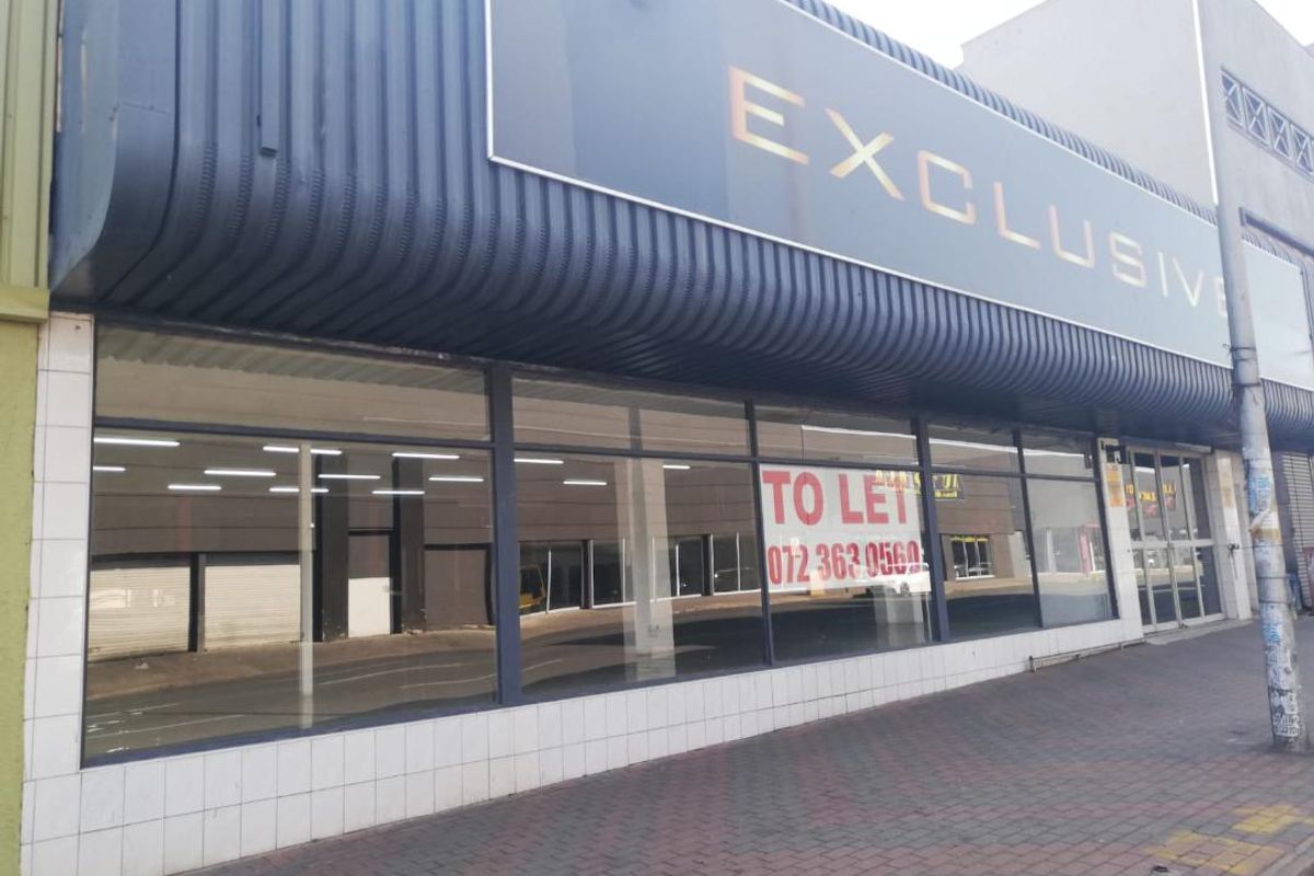 Street-level commercial storefront featuring large display windows, metal cladding, and prominent signage, suitable for retail or office use.