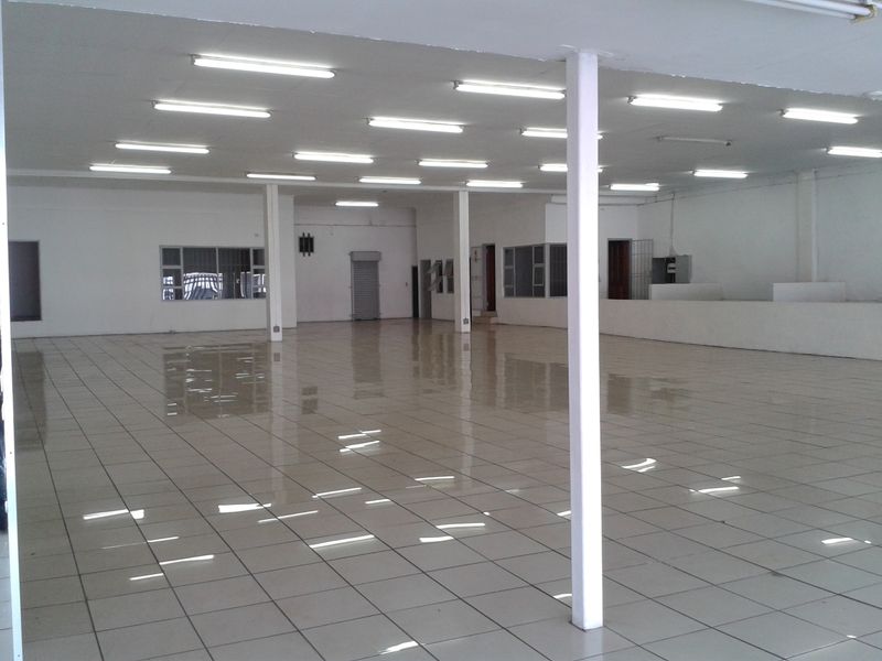 A spacious, open-plan commercial interior featuring tiled flooring, structural support columns, and overhead fluorescent lighting, suitable for retail or office use.