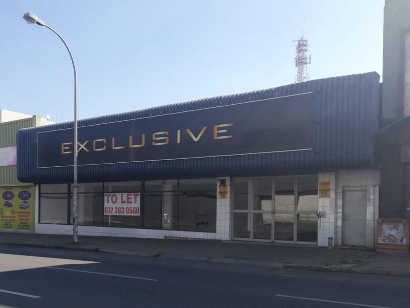 Street-facing commercial storefront featuring large display windows, prominent signage, and a paved entrance area, suitable for retail or office use.