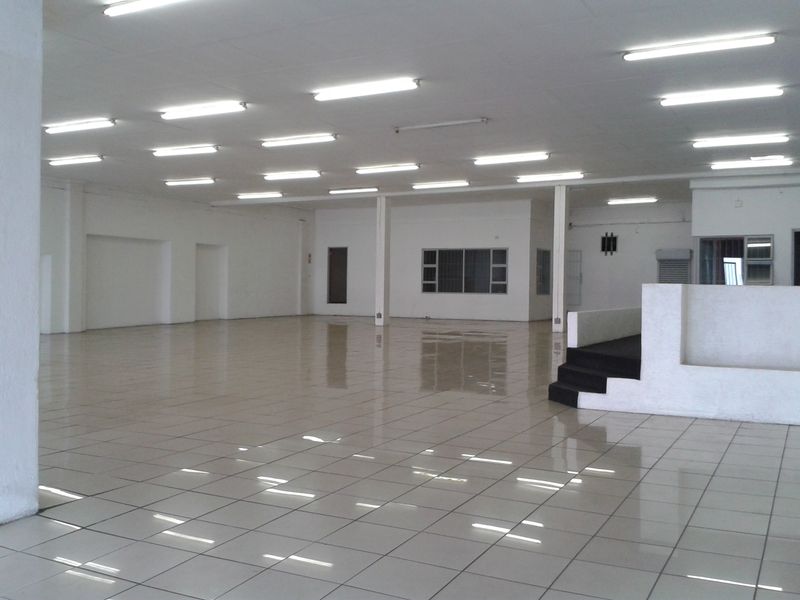 A spacious, open-plan commercial interior featuring tiled flooring, recessed lighting, and a raised platform area, suitable for various business or retail configurations.