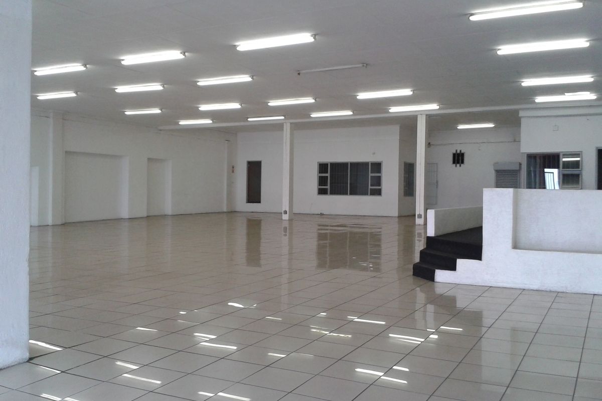 A spacious, open-plan commercial interior featuring tiled flooring, recessed lighting, and a raised platform area, suitable for various business or retail configurations.
