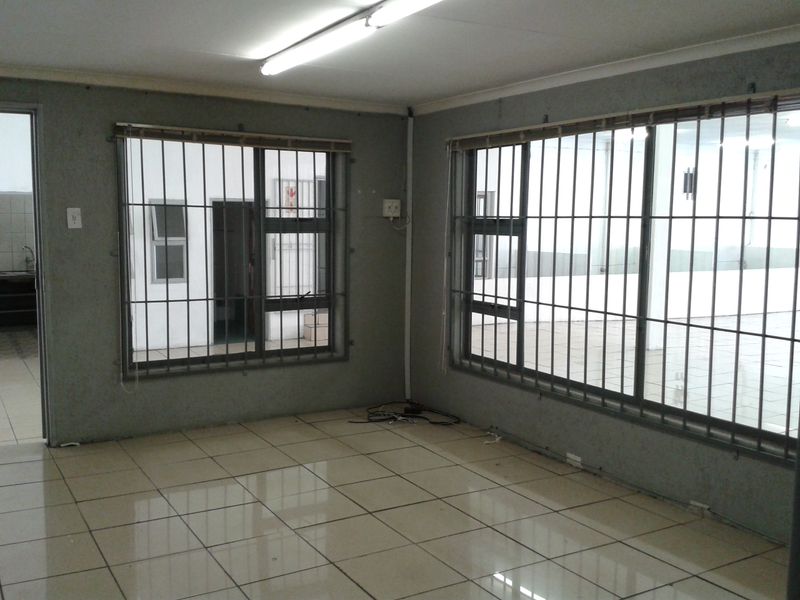 An empty office or commercial space featuring tiled flooring, large windows with security bars, and fluorescent overhead lighting.