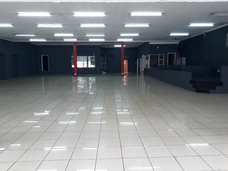 Spacious open-plan commercial interior featuring tiled flooring, recessed fluorescent lighting, and a raised platform area, suitable for retail or office use.