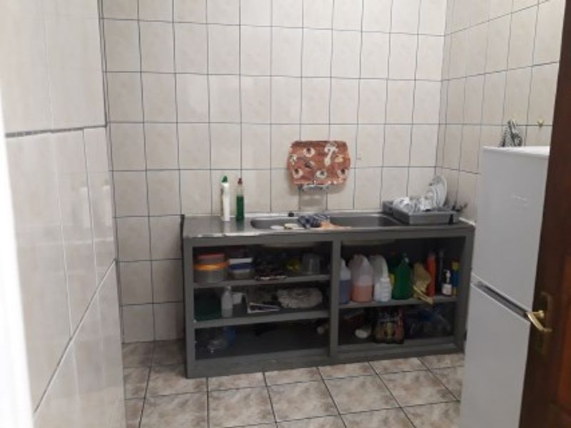 A functional laundry or utility area featuring a built-in stainless steel sink unit with open shelving and full-height wall tiling.