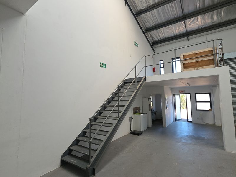 Spacious industrial warehouse unit featuring a mezzanine level, metal staircase, roller shutter door, and high-clearance exposed roof structure.