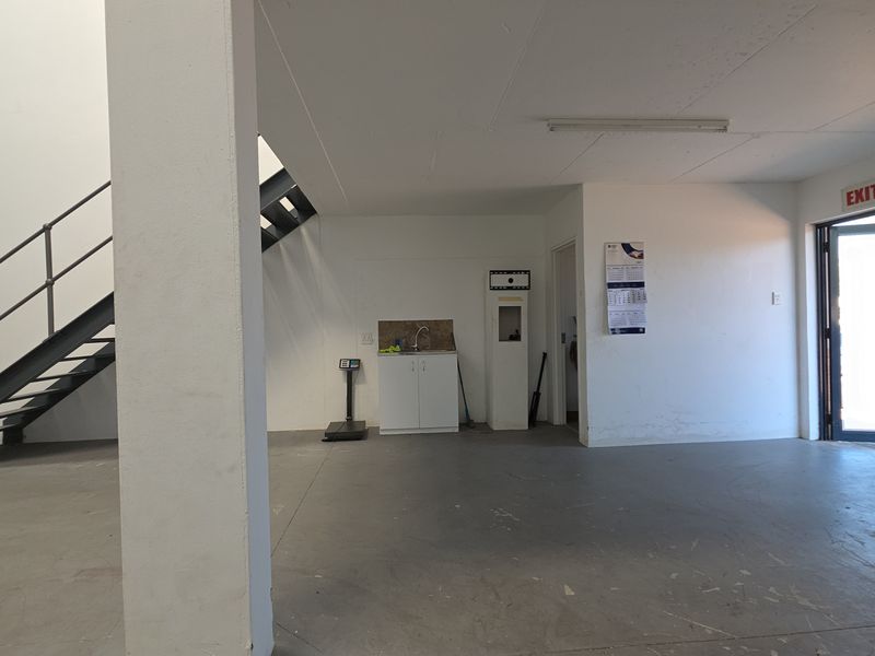 Open-plan industrial utility space featuring a metal staircase, concrete flooring, and a small built-in sink unit with direct exit access.