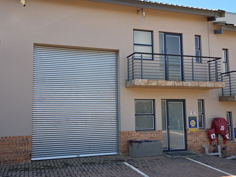 Front elevation of an industrial property featuring large roller shutter doors, upper-level balconies, and paved access area.