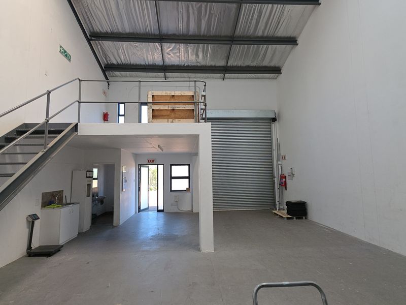 Spacious industrial warehouse unit featuring a mezzanine level, roller shutter door access, high ceilings, and a small kitchenette area.