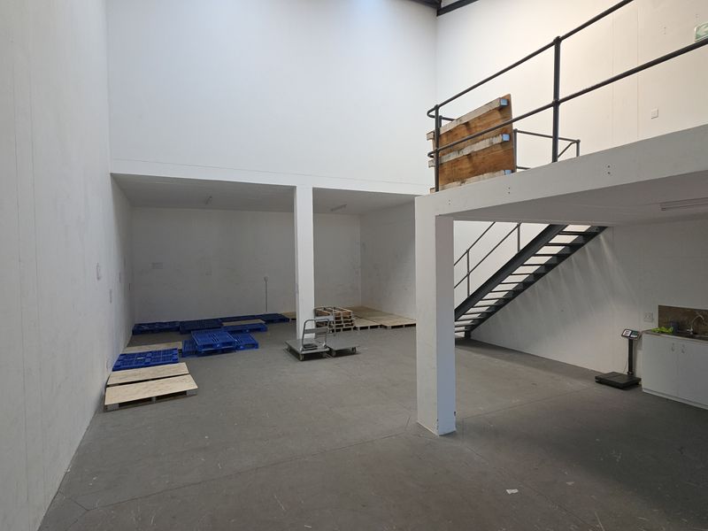 Spacious industrial utility area featuring a mezzanine level with metal staircase, high ceilings with skylight, and a compact kitchenette sink unit.