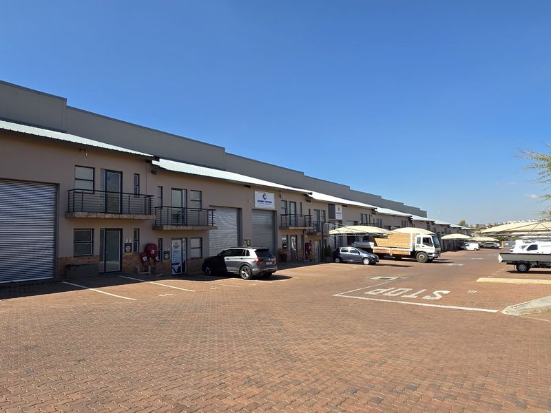 A wide-angle view of an industrial park featuring multiple units with roller shutter doors, balconies, and a paved common driveway area.