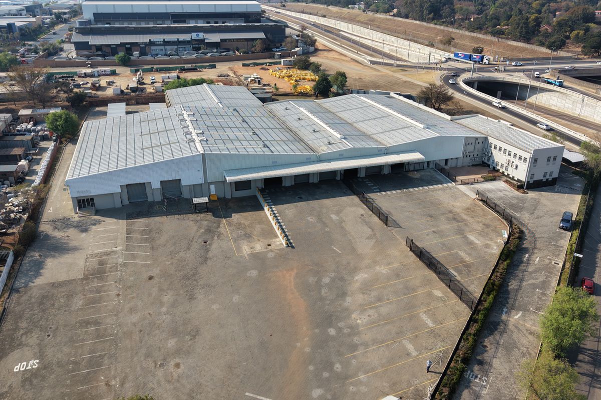 Aerial view of a large industrial warehouse facility featuring extensive loading bays, a paved parking yard, and an attached office building.