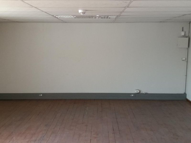 An empty industrial office space featuring timber flooring, a suspended ceiling, and exposed electrical infrastructure.