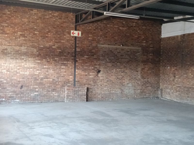 Spacious industrial utility area featuring exposed brick walls, concrete flooring, and high-clearance steel roof trusses, equipped with essential fire safety infrastructure.