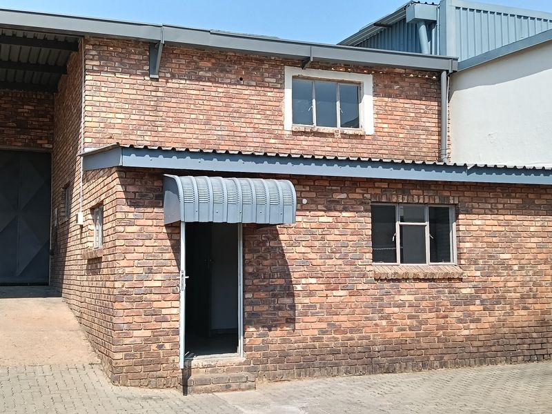 Industrial property exterior featuring face brick construction, a large roller shutter door, and a paved entrance area with a metal awning.