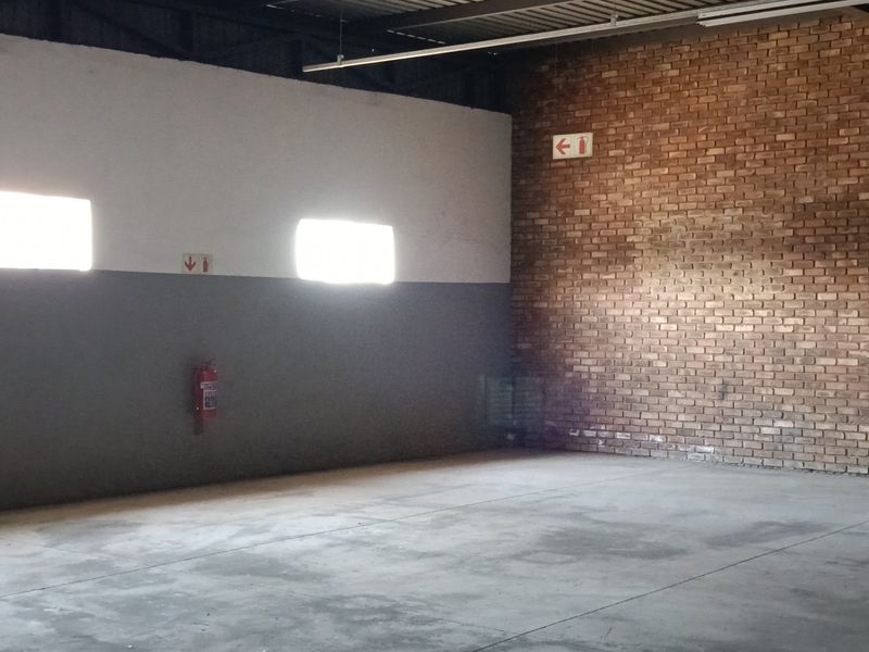 Spacious industrial utility area featuring exposed brickwork, concrete flooring, and high steel roof trusses, suitable for storage or workshop operations.