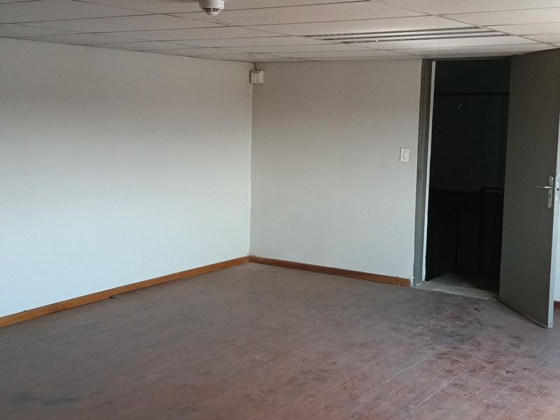 An empty industrial office space featuring timber flooring, a suspended ceiling, and a single internal access door.