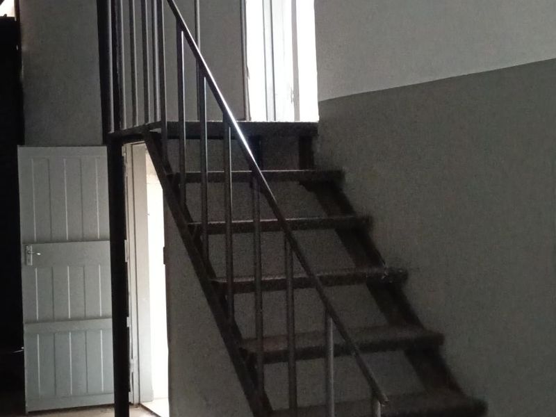 An industrial utility space featuring a metal staircase, exposed roof structure, and access doors, suitable for storage or workshop use.