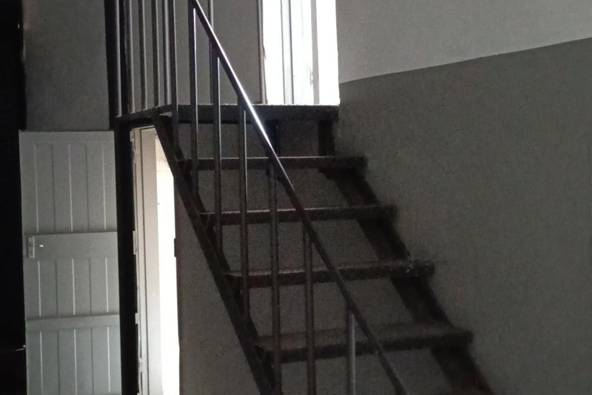 An industrial utility space featuring a metal staircase, exposed roof structure, and access doors, suitable for storage or workshop use.