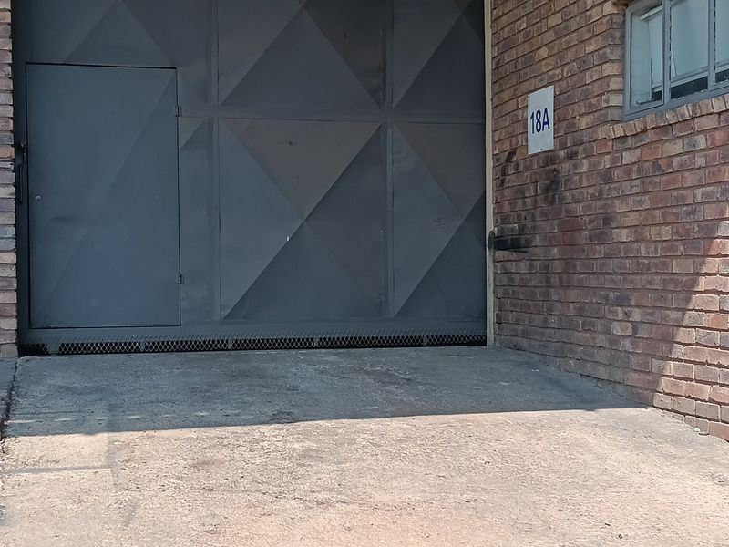 Industrial unit entrance featuring a large roller shutter door, brick facade, and concrete driveway access.