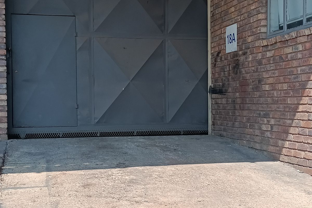 Industrial unit entrance featuring a large roller shutter door, brick facade, and concrete driveway access.