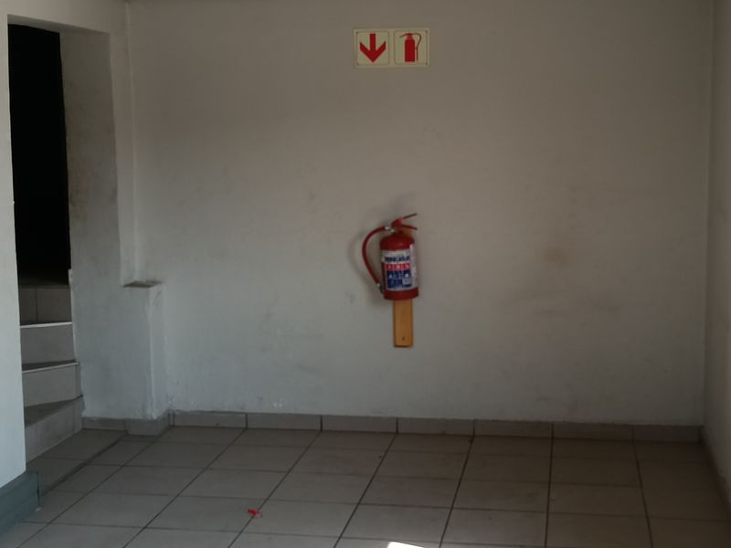 An empty utility space featuring tiled flooring, steel frame windows, and wall-mounted fire safety equipment.