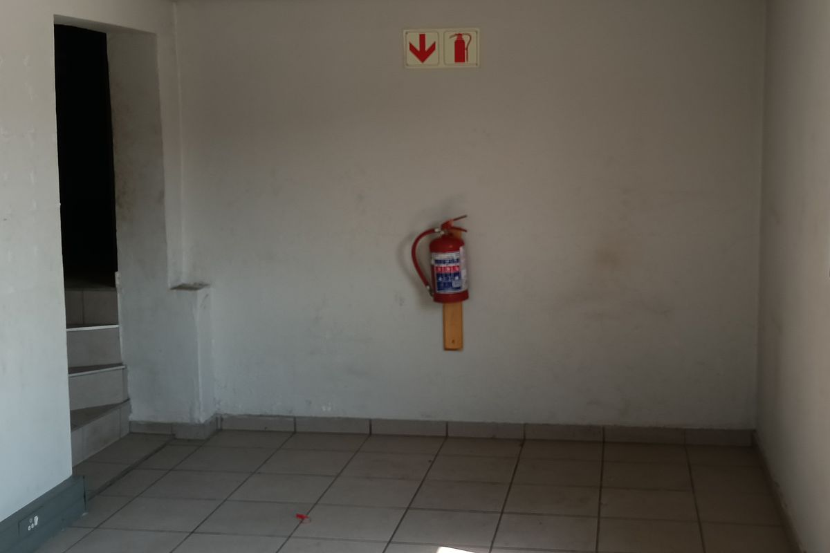 An empty utility space featuring tiled flooring, steel frame windows, and wall-mounted fire safety equipment.