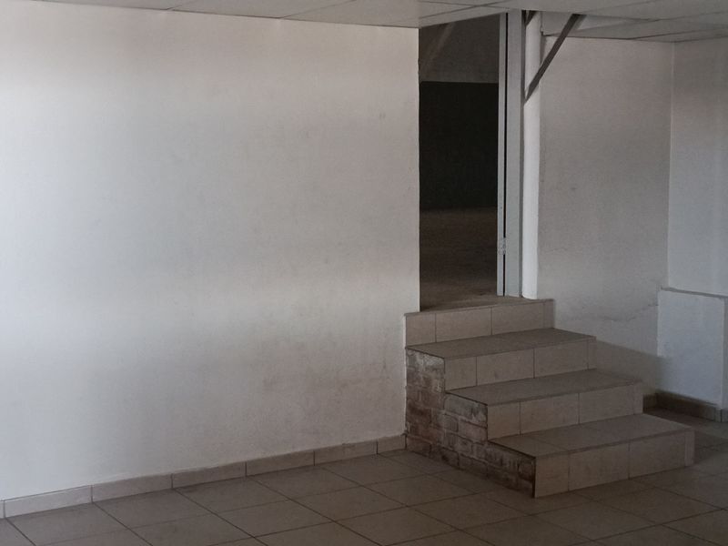 An empty industrial utility space featuring tiled flooring, a tiled staircase, and a suspended ceiling, suitable for various commercial or storage applications.