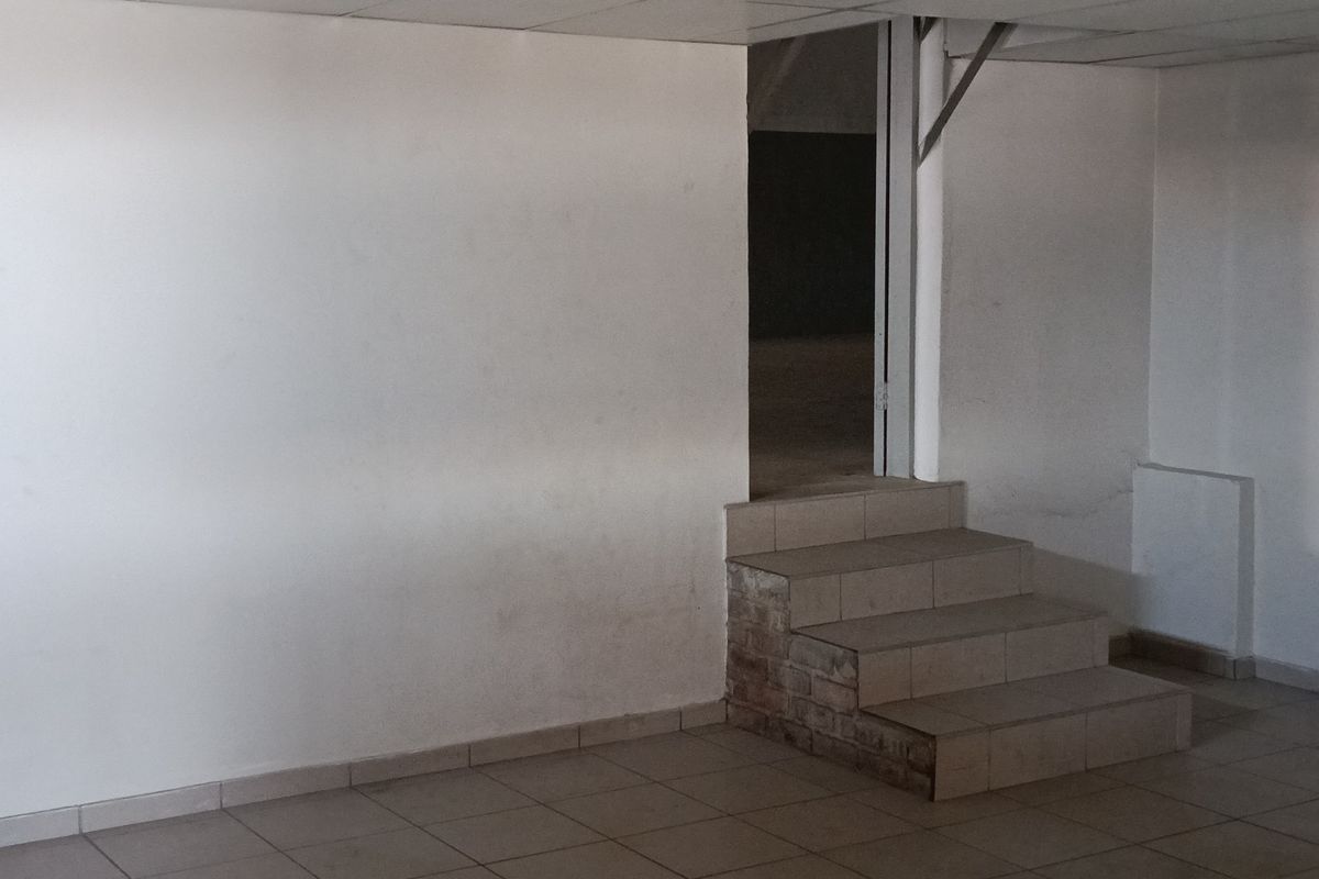 An empty industrial utility space featuring tiled flooring, a tiled staircase, and a suspended ceiling, suitable for various commercial or storage applications.