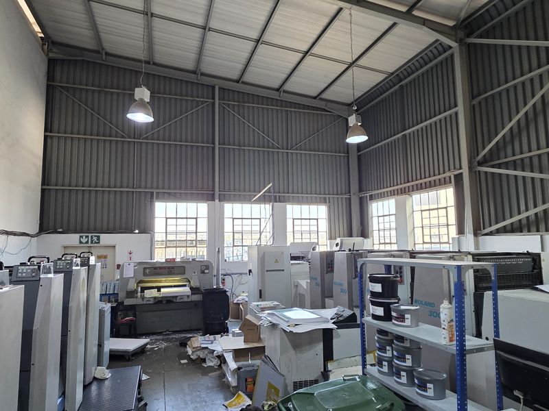 Spacious industrial utility area featuring high ceilings with exposed steel trusses, corrugated metal walls, and large industrial windows providing natural light.