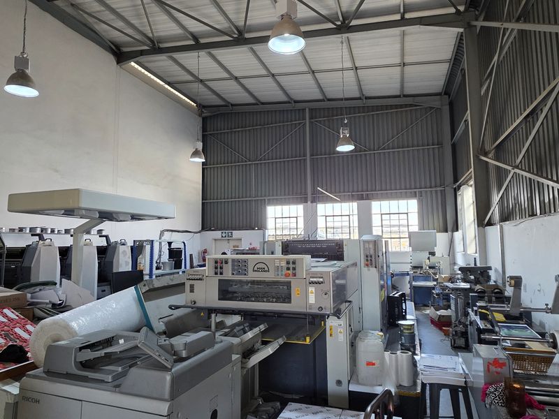 Spacious industrial warehouse unit featuring high-bay ceilings, exposed steel roof trusses, and functional industrial lighting, suitable for manufacturing or storage operations.