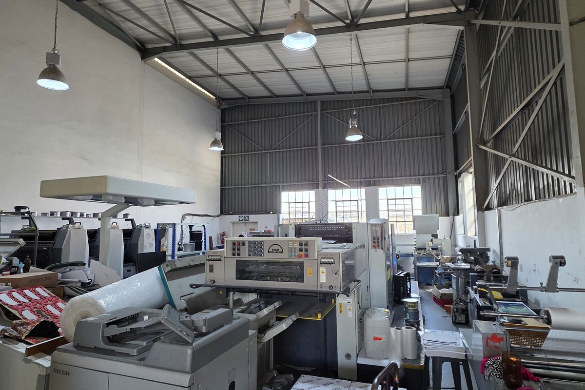 Spacious industrial warehouse unit featuring high-bay ceilings, exposed steel roof trusses, and functional industrial lighting, suitable for manufacturing or storage operations.