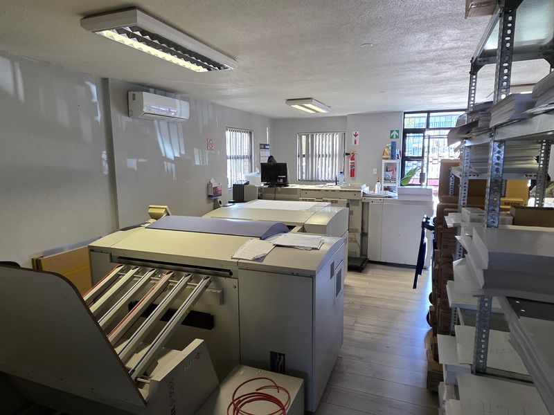 Functional industrial utility or printing workspace featuring laminate flooring, air conditioning, and overhead fluorescent lighting.