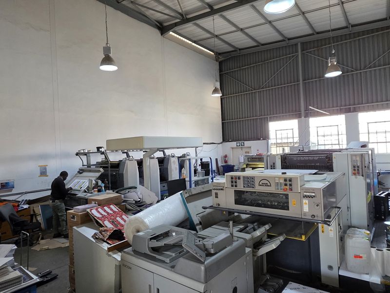 Spacious industrial utility area featuring high-bay ceilings, exposed steel roof structure, and integrated industrial printing machinery.