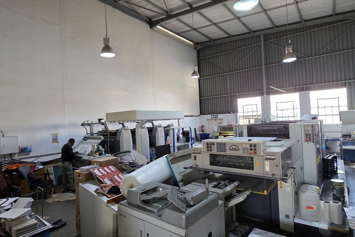 Spacious industrial utility area featuring high-bay ceilings, exposed steel roof structure, and integrated industrial printing machinery.