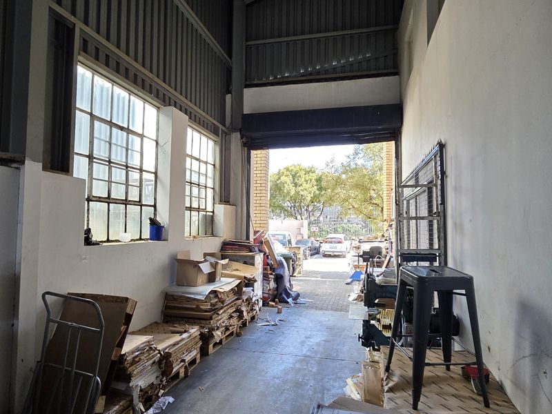 Industrial utility space featuring high ceilings, exposed steel structure, large steel-framed windows, and a wide roller shutter door providing direct access to the exterior.