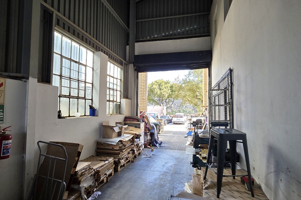 Industrial utility space featuring high ceilings, exposed steel structure, large steel-framed windows, and a wide roller shutter door providing direct access to the exterior.