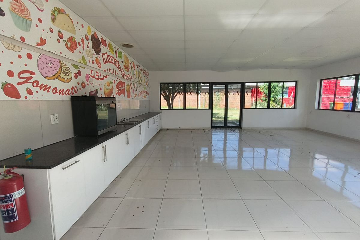 Spacious industrial kitchen area featuring white cabinetry, granite countertops, tiled flooring, and large windows providing ample natural light.