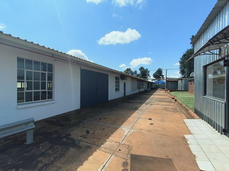 Exterior view of an industrial property featuring a long concrete yard, corrugated metal cladding, and large industrial access doors.