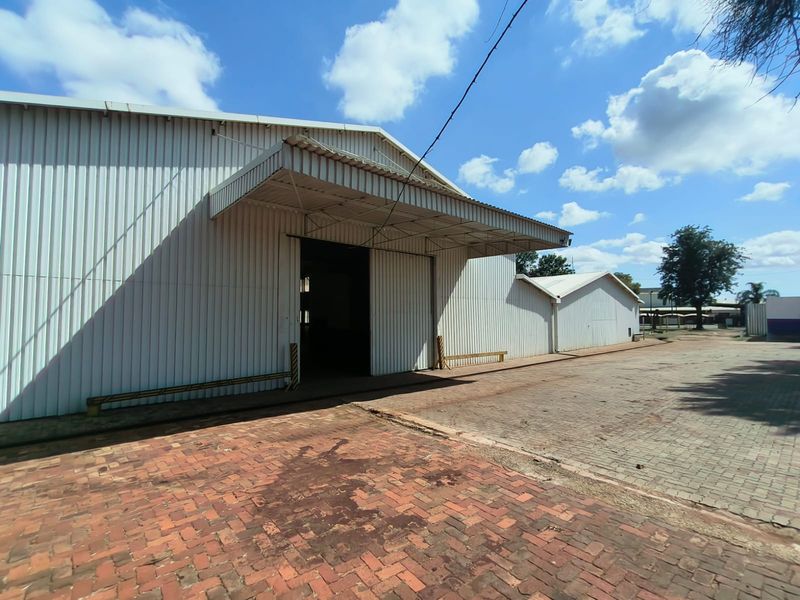 Industrial warehouse exterior featuring corrugated metal cladding, a covered loading bay area, and extensive brick-paved yard space.