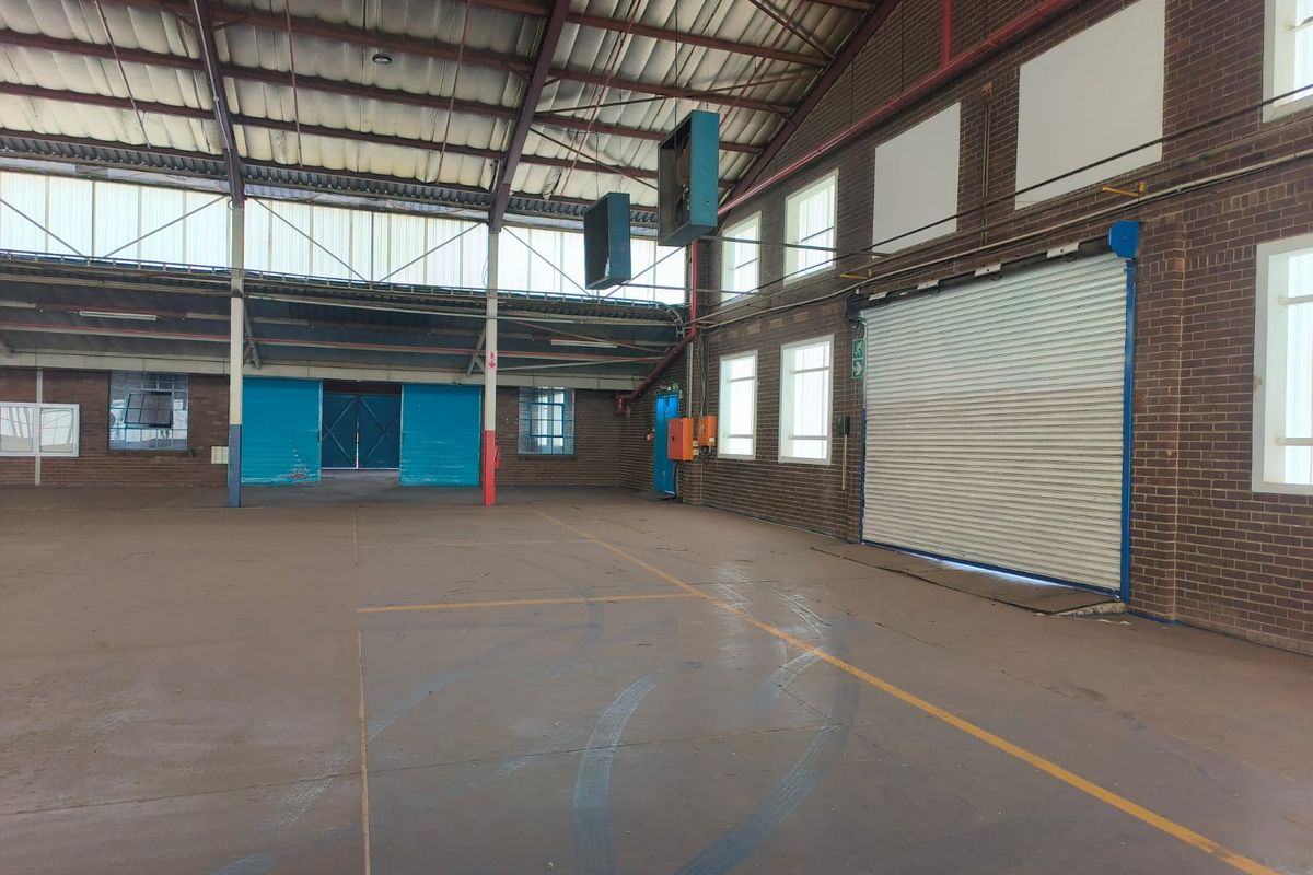 Spacious industrial warehouse featuring high ceilings with exposed steel trusses, concrete flooring, and a large roller shutter door for easy access.