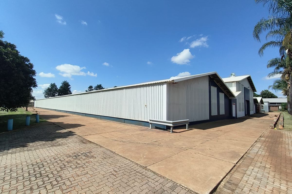 Exterior view of a large industrial warehouse building featuring corrugated metal cladding, a concrete apron, and paved driveway access.